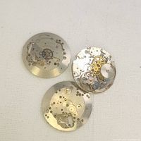Three Swiss watch movement parts arranged on a light background showing various gears and mechanical components.