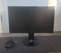 Front view of ASUS VG248QE gaming monitor with power cable coiled beside it on the floor.