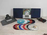 Front view of Centrios vertical CD player/radio with blue speaker fabric, showing mixed CDs and accessories with detachable stand and power cord.