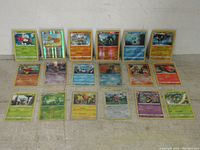 Front view of 14 assorted holographic Pokemon cards arranged in 2 rows showing various Pokemon characters and types.