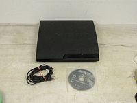 Black PlayStation 3 console with matching power cord and Reflex MX ATV game disc lying flat on a light-colored surface.