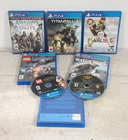 Photo shows five PS4 game cases and two discs out of cases, along with an additional empty case with a card inside.