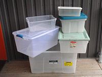 Overview of six Rubbermaid storage bins of various sizes stacked and grouped together on wooden floor, some bins have lids with different colors.