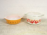 Two vintage Pyrex dishes side by side on a beige surface, smaller orange dish with brown Friendship pattern and larger white dish with red Town and Country pattern with lid