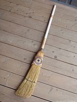 Vintage Sharpshooter corn broom curling brush with wooden handle wrapped in white grip tape, shown full length on wooden floor.