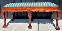 Front view of bench showing dark wood carved legs and apron with ball and claw feet. Upholstered seat with blue striped fabric visible.