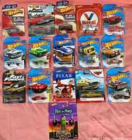 Full lot of 16 diecast Hot Wheels cars in original sealed packaging, arranged on pink surface.