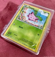 Front view of clear protective plastic box containing a stack of Pokemon trading cards, showing a front card featuring Hoppip.