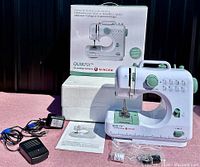 Singer QuikFix sewing machine displayed outside the original box with included power adapter, foot pedal, instruction manual, and accessories in plastic bags to show complete lot.