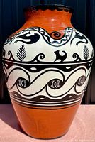 Front view of large handmade pottery vase showing terracotta base color with black and white painted stylized eye and animal patterns.