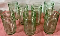 View showing all seven green tinted Anchor Hocking glasses with their concentric ring texture visible, arranged in a group on a pink cloth.