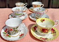 Front angle photo showing six vintage bone china cups and saucers with various floral patterns and gilt edges.