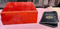 Photo of the wooden cigar humidor box and black fabric carrying case side by side on a pink surface under natural light.