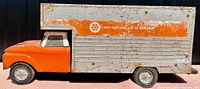 Side view of orange and gray steel toy moving van showing truck body with 'One-Way And Local Rentals' on side and visible rust and paint wear.