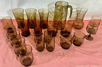 Collection displayed on pink cloth, includes assorted smoked glass glasses, cups, a pitcher, and a vase grouped together.