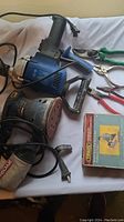 View of electric sanders, pliers, and boxed router bit set spread on a white surface