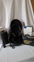 Overview photo showing Bluetooth speaker, headphones in case, boxed security light bulb camera, memory card reader, and charging block