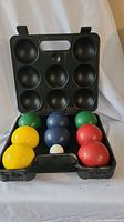 Open black plastic carrying case with eight large bocce balls in yellow, green, blue, and red and one small white pallino ball displayed inside.