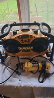 Front view of the yellow and black DeWalt work site radio and the yellow corded DeWalt cut out tool with power cords on a table.