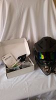 Full view of the black full face off-road motorcycle helmet with a reflective multicolor tinted visor next to the open box containing the Lexin ET COM motorcycle Bluetooth intercom kit and user guide.
