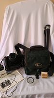 Full view of Nikon D90 camera with lens, battery grip, green Lowepro camera bag, Nikon eyepiece box, lens cap, camera manual, and black cylindrical accessory case.