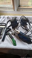 Photo showing two electric handheld sanders, multi-tool oscillating tool, hand scrapers, and drill bit set on a white cloth under a window.