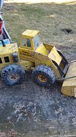 Full side view of the Tonka Mighty Loader showing the large tires, cabin, and front loader bucket with dirt and wear marks visible on the yellow paint.