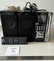 Front view of Aiwa micro Hi-Fi system including main unit with display, two speakers with black mesh grills, remote control, speaker wires laid on top and nearby.