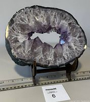 Front view of large natural amethyst crystal geode slice on stand showing hollow crystalline center and purple shades.