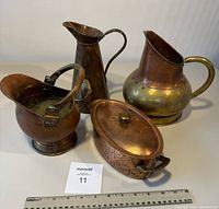 Photo showing all four antique items: Joseph Sankey copper pitcher, brass and copper pitcher, copper gravy boat, and copper terrine dish with lid, positioned with ruler for scale.