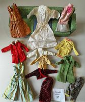 Photo of assortment of Barbie doll clothing and green patterned doll furniture case including a couch and armchair