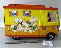 Side view of Barbie Country Camper toy in bright yellow and orange with rainbow and flower decals, showing wheels and camper body.