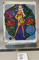 Closed view of the Barbie doll carrying case featuring a colorful illustration of Barbie in a striped dress with floral motifs around her.