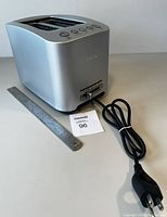 Full view of the Breville brushed stainless steel toaster from side with power cord laid out. A ruler is present for size context.