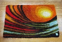 Top view of vibrant carpet laid flat on wooden floor showing swirling bands of color and rising sun design.