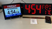 Front view of two digital timekeeping devices: left is an 8" digital calendar day clock showing day, period of day, time, and date with color display; right is a large red 16.5" LED digital wall clock showing time, day, date and temperature.