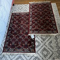 Two small Persian style area rugs placed side by side on hardwood floor, one slightly overlapping the other. Both have dark red floral geometric designs and beige fringes.