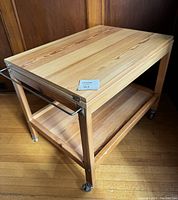 Side view of blonde wood two-tiered trolley showing hinged top closed and stainless steel towel bar on side.