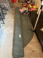 Rolled braided area rug partly unrolled on concrete floor near treadmill and storage items.