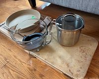 View of all items on wooden floor including deep dish baker on box, glass pourer, stainless pot, baking stone