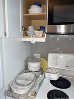 Photo showing stacked French White ribbed casserole dishes with clear glass lids, some oval white porcelain dishes, and a Cornflower Blue patterned casserole on the stove