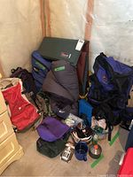 Overall lot showing various backpacks, sleeping bags, Therm-a-Rest mat, cooking supplies including pot and utensils, and Camelbak pouch.