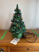 Front view of green ceramic Christmas tree lit ornament decor with brown electric cord and two-prong plug.