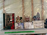 Four Christmas village buildings displayed in original packaging, showing lighthouse, pharmacy, and other buildings in the lot.
