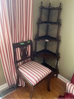 Wooden chair with striped cushion seat in front of red and white striped curtains, next to wooden corner shelf