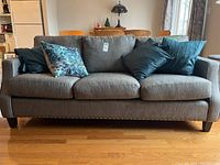 Front view of grey three-seater couch with four throw pillows on hardwood floor