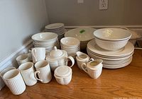 Full set of stacked plates, bowls, mugs, teapot, and cream and sugar on wooden surface