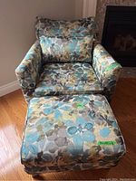 Front view of floral armchair with matching ottoman on hardwood floor by fireplace.