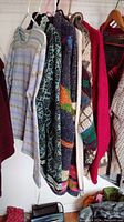 Photo showing six different ladies sweaters and cardigans hanging on a rod, various colors and patterns including a zip-up cardigan and multi-colored geometirc knit.