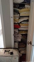 Closed linen closet door with visible stacked linens including towels and folded sheets, plus a packaged double bed duvet on floor.